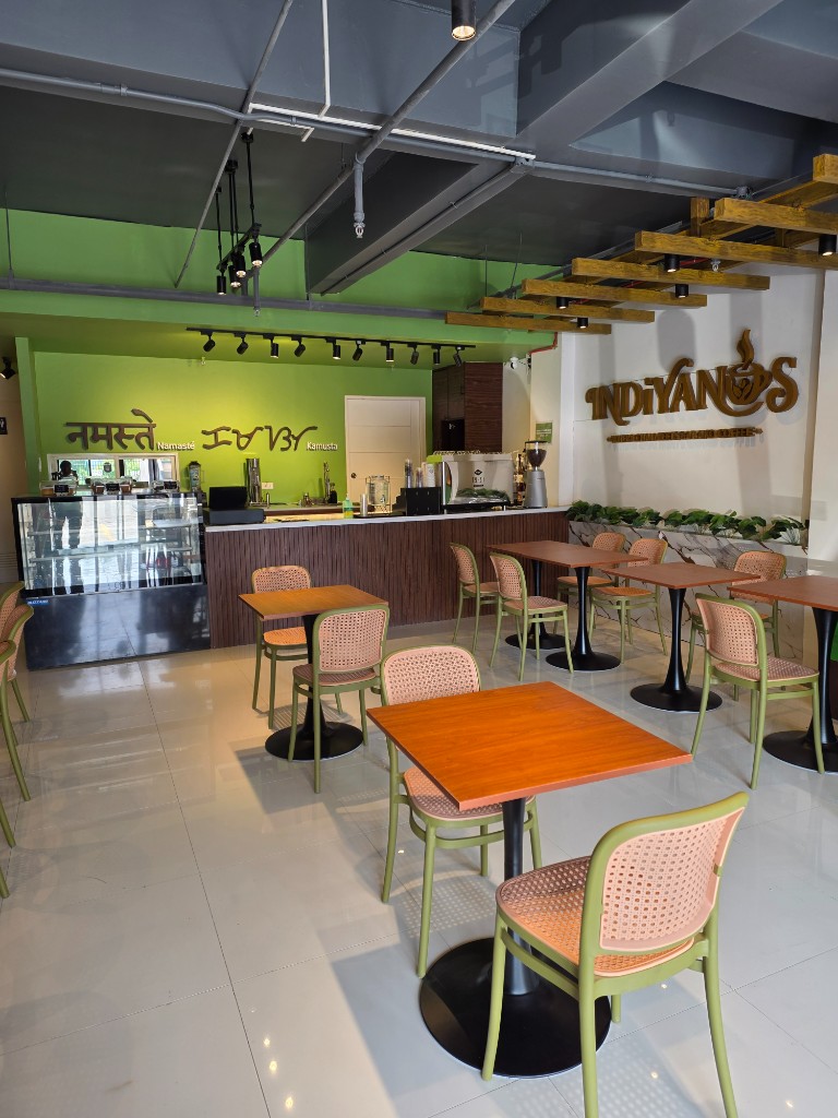 Inside Indiyanos — seating, wooden Indiyanos wall sign, and Namaste Kamusta mural